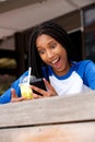 Young african american woman sitting at cafe looking at mobile phone with surprised expression Royalty Free Stock Photo