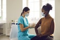 Young African-American woman sitting at doctor's office and getting a shot in her arm Royalty Free Stock Photo