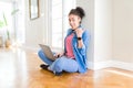 Young african american woman sitting on the floor using computer laptop pointing and showing with thumb up to the side with happy Royalty Free Stock Photo