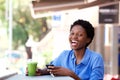 Young african american woman sitting at outdoor cafe with a mobile phone and laughing Royalty Free Stock Photo