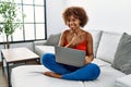 Young african american woman sitting on the sofa at home using laptop cheerful with a smile of face pointing with hand and finger Royalty Free Stock Photo