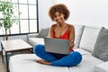 Young african american woman sitting on the sofa at home using laptop happy face smiling with crossed arms looking at the camera Royalty Free Stock Photo