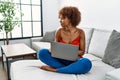 Young african american woman sitting on the sofa at home using laptop looking to side, relax profile pose with natural face with Royalty Free Stock Photo