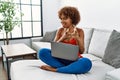 Young african american woman sitting on the sofa at home using laptop pointing fingers to camera with happy and funny face Royalty Free Stock Photo