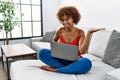 Young african american woman sitting on the sofa at home using laptop smiling cheerful presenting and pointing with palm of hand Royalty Free Stock Photo