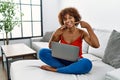 Young african american woman sitting on the sofa at home using laptop smiling cheerful showing and pointing with fingers teeth and Royalty Free Stock Photo