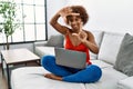 Young african american woman sitting on the sofa at home using laptop smiling making frame with hands and fingers with happy face Royalty Free Stock Photo