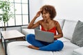Young african american woman sitting on the sofa at home using laptop very happy and smiling looking far away with hand over head Royalty Free Stock Photo