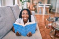Young african american woman smiling happy laying on the sofa reading book at home Royalty Free Stock Photo
