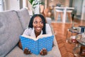 Young african american woman smiling happy laying on the sofa reading book at home