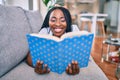 Young african american woman smiling happy laying on the sofa reading book at home Royalty Free Stock Photo