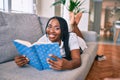 Young african american woman smiling happy laying on the sofa reading book at home