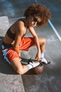 Young african-american woman in sportive attire and high heels sitting on bench with basketball ball under Royalty Free Stock Photo