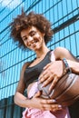 young african-american woman in sports bra and pink overalls holding basketball ball and leaning Royalty Free Stock Photo