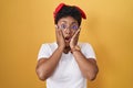 Young african american woman standing over yellow background afraid and shocked, surprise and amazed expression with hands on face Royalty Free Stock Photo