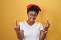 Young african american woman standing over yellow background showing middle finger doing fuck you bad expression, provocation and Royalty Free Stock Photo