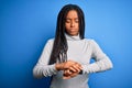 Young african american woman standing wearing casual turtleneck over blue isolated background Checking the time on wrist watch, Royalty Free Stock Photo