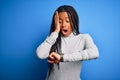 Young african american woman standing wearing casual turtleneck over blue isolated background Looking at the watch time worried, Royalty Free Stock Photo