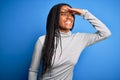 Young african american woman standing wearing casual turtleneck over blue isolated background very happy and smiling looking far Royalty Free Stock Photo