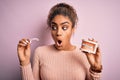 Young african american woman surprised and shocked holding professional orthodontic denture with metal braces and removable