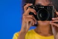 Young african american woman takes pictures with DSLR camera on blue background in studio. Girl smiling as photographer. Royalty Free Stock Photo