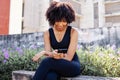 Young African American woman using a mobile phone and sitting on bench in the park. Female black jogger resting and Royalty Free Stock Photo