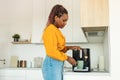 Young african american woman using modern coffee machine, making drink in the morning, standing in kitchen at home Royalty Free Stock Photo