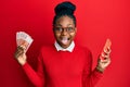 Young african american woman using smartphone holding norwegian krone banknotes celebrating crazy and amazed for success with open Royalty Free Stock Photo