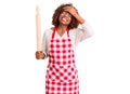 Young african american woman wearing apron holding rolling pin stressed and frustrated with hand on head, surprised and angry face Royalty Free Stock Photo