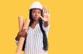 Young african american woman wearing architect hardhat holding blueprints with open hand doing stop sign with serious and Royalty Free Stock Photo