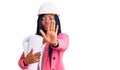 Young african american woman wearing architect hardhat holding blueprints with open hand doing stop sign with serious and Royalty Free Stock Photo