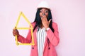 Young african american woman wearing bike helmet and holding water bottle covering mouth with hand, shocked and afraid for mistake