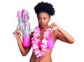 Young african american woman wearing bikini and hawaiian lei holding water gun with angry face, negative sign showing dislike with Royalty Free Stock Photo