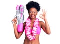 Young african american woman wearing bikini and hawaiian lei holding water gun doing ok sign with fingers, smiling friendly Royalty Free Stock Photo