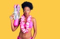 Young african american woman wearing bikini and hawaiian lei holding water gun scared and amazed with open mouth for surprise, Royalty Free Stock Photo