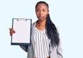 Young african american woman wearing business clothes holding clipboard thinking attitude and sober expression looking self Royalty Free Stock Photo