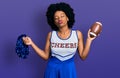 Young african american woman wearing cheerleader uniform holding pompom and football ball looking at the camera blowing a kiss