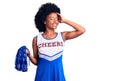 Young african american woman wearing cheerleader uniform holding pompom smiling confident touching hair with hand up gesture, Royalty Free Stock Photo