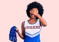 Young african american woman wearing cheerleader uniform holding pompom smiling and laughing with hand on face covering eyes for Royalty Free Stock Photo