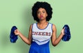 Young african american woman wearing cheerleader uniform using pompom puffing cheeks with funny face