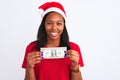 Young african american woman wearing christmas hat and holding one dollar banknote with a happy face standing and smiling with a Royalty Free Stock Photo