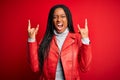 Young african american woman wearing cool fashion leather jacket over red isolated background shouting with crazy expression doing Royalty Free Stock Photo