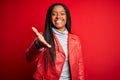 Young african american woman wearing cool fashion leather jacket over red isolated background smiling friendly offering handshake