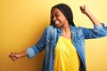 Young african american woman wearing denim shirt standing over isolated yellow background Dancing happy and cheerful, smiling Royalty Free Stock Photo