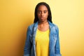 Young african american woman wearing denim shirt standing over isolated yellow background Relaxed with serious expression on face Royalty Free Stock Photo