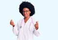 Young african american woman wearing doctor coat and stethoscope doing money gesture with hands, asking for salary payment, Royalty Free Stock Photo