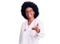 Young african american woman wearing doctor coat and stethoscope smiling cheerful offering palm hand giving assistance and Royalty Free Stock Photo