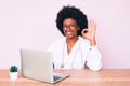 Young african american woman wearing doctor stethoscope working using computer laptop doing ok sign with fingers, smiling friendly Royalty Free Stock Photo