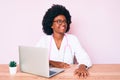 Young african american woman wearing doctor stethoscope working using computer laptop looking away to side with smile on face, Royalty Free Stock Photo