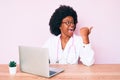 Young african american woman wearing doctor stethoscope working using computer laptop pointing thumb up to the side smiling happy Royalty Free Stock Photo